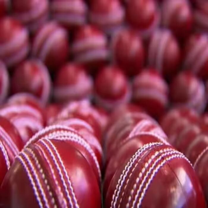 Red leather cricket ball, showing hand-stitched seam and glossy finish.